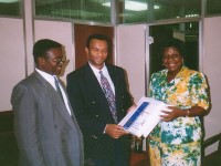 A man and woman present an award to a 2nd man